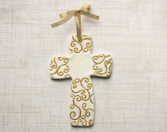 May include: White ceramic cross with gold swirl design. The cross has a gold ribbon attached to the top.