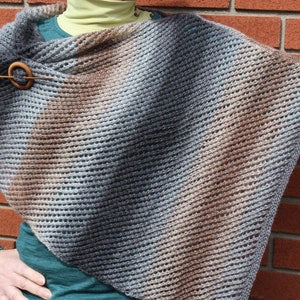 May include: A gray, brown, and blue striped knitted shawl with a wooden pin.