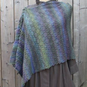 May include: A blue, green and purple knitted shawl with a lacy pattern. The shawl is draped over a mannequin wearing a dark grey dress.