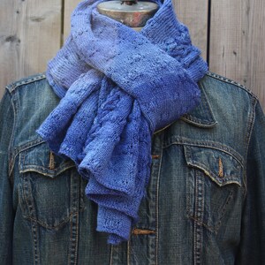 May include: A blue knitted scarf with a gradient of color from light to dark blue. The scarf is draped over a denim jacket.