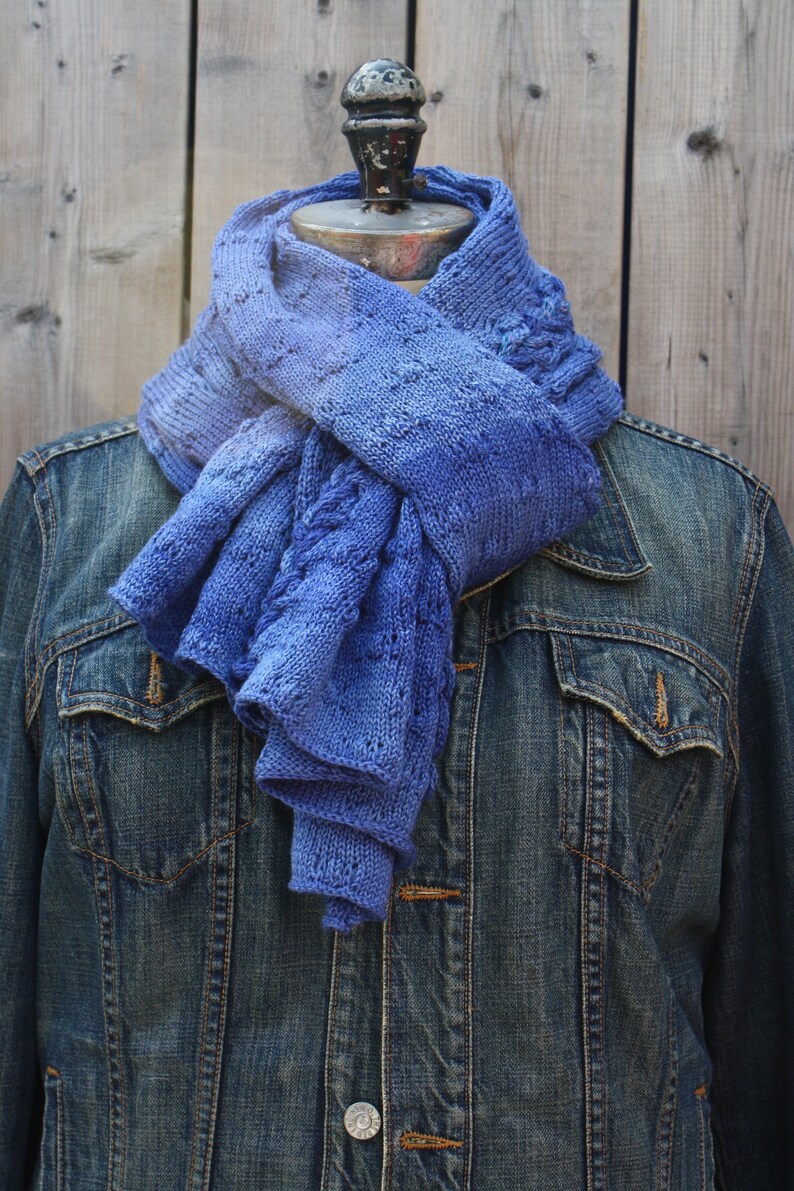 May include: A blue knitted scarf with a gradient of color from light to dark blue. The scarf is draped over a denim jacket.