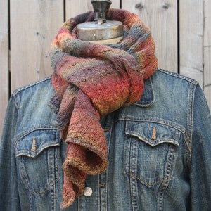 May include: A multi-colored scarf with shades of red, orange, brown, and gray, draped around a denim jacket.