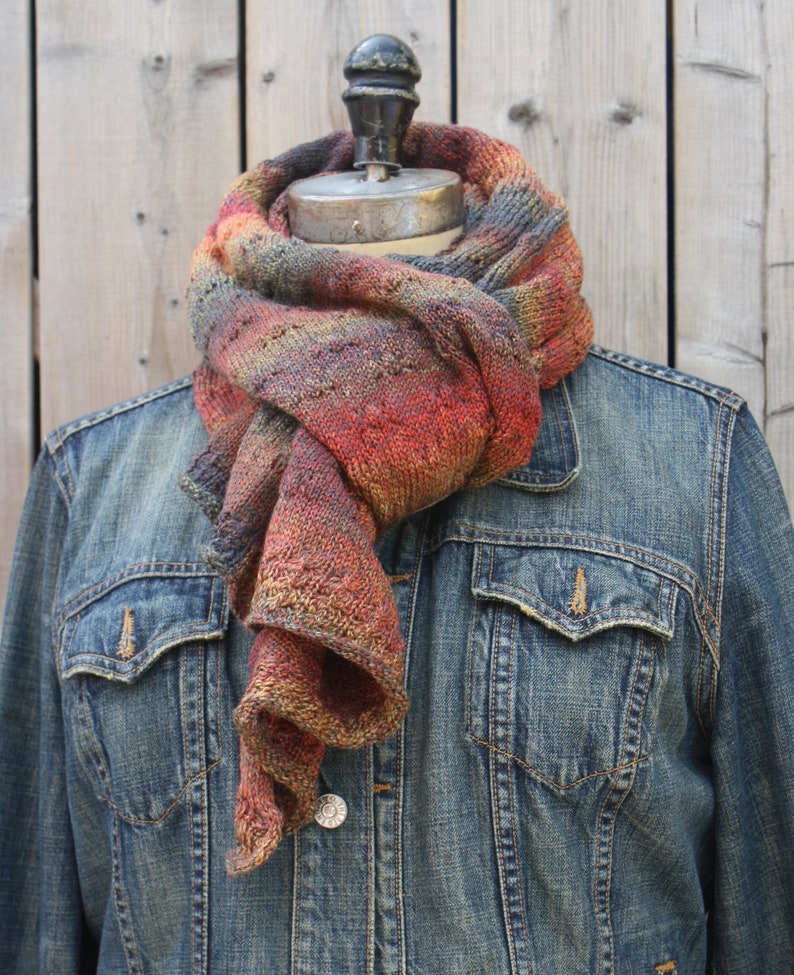 May include: A multi-colored scarf with shades of red, orange, brown, and gray, draped around a denim jacket.