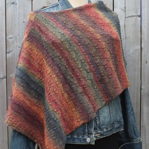 May include: A striped knit shawl in shades of red, orange, brown, and gray. The shawl is draped over a mannequin wearing a denim jacket and a black skirt.