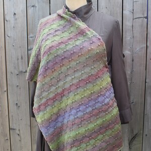 May include: A multi-colored knitted shawl with a textured pattern. The shawl is draped over a mannequin wearing a brown shirt.