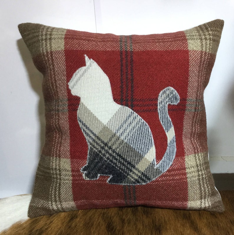 May include: Square decorative pillow with a red plaid pattern and a white cat silhouette. The cat is filled with a plaid pattern in shades of gray, beige, and navy blue. The pillow has a soft, textured appearance.