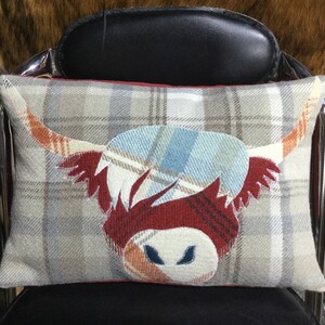 May include: A decorative pillow with a plaid pattern featuring a red, white, and blue Highland cow design.