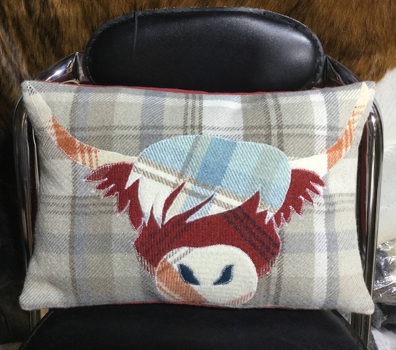 May include: A decorative pillow with a plaid pattern featuring a red, white, and blue Highland cow design.