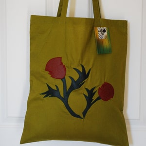 May include: A green canvas tote bag with a black and red leather applique of a stylised flower. The bag has two long straps.