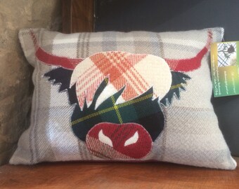 May include: A gray and white plaid pillow with a red, orange, green, and black highland cow design. The pillow is made of wool and has a fringed edge.