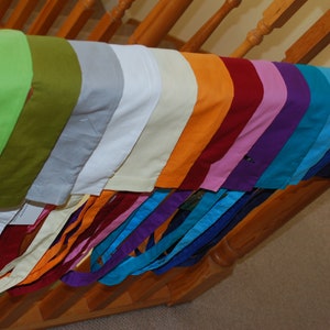 May include: A collection of fabric scraps in various colours, including green, olive, grey, white, cream, orange, red, pink, purple, blue, teal, and black. The fabric scraps are arranged in a rainbow pattern and are hanging from a wooden railing.