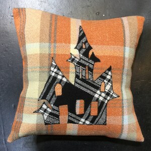 May include: Orange and white plaid throw pillow with a black and white applique of a haunted house.