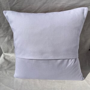 May include: A square, white pillow with a simple design. The pillow has a solid white front and a back with a flap opening. The pillow is made of a soft, likely cotton, fabric.