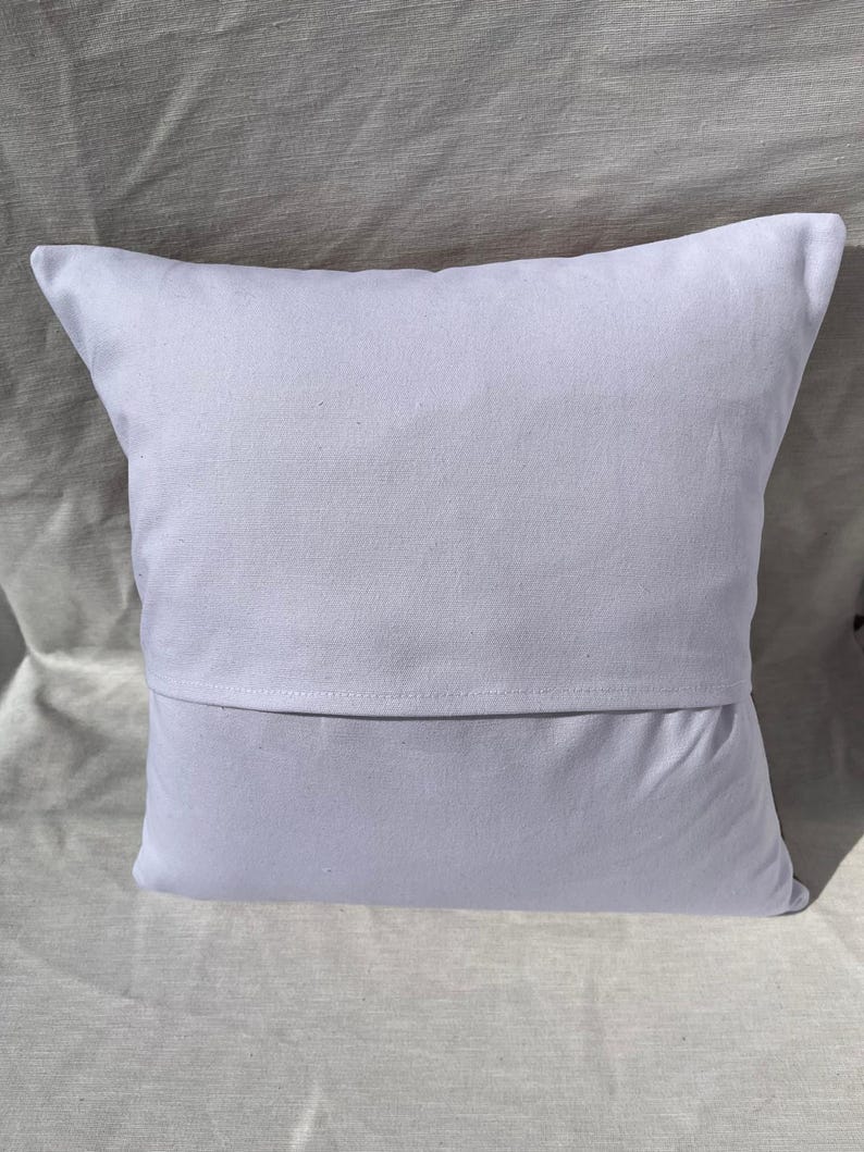 May include: A square, white pillow with a simple design. The pillow has a solid white front and a back with a flap opening. The pillow is made of a soft, likely cotton, fabric.