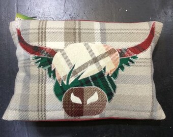 May include: A beige and brown plaid pillow with a red and green embroidered Highland cow design.