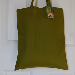 May include: A green canvas tote bag with a small tag attached to the handle. The tag has a picture of a butterfly and the text "Handmade with Love".