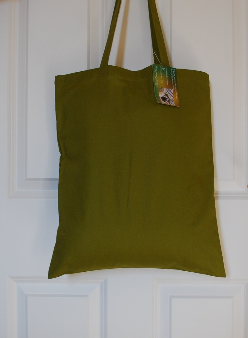 May include: A green canvas tote bag with a small tag attached to the handle. The tag has a picture of a butterfly and the text "Handmade with Love".