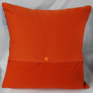 May include: Orange pillow with a hidden zipper closure and a button on the back. The pillow is made of a soft, comfortable fabric.