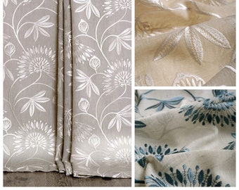 May include: Three fabric swatches with a floral pattern. The first swatch is a light beige with white floral embroidery. The second swatch is a light beige with white floral embroidery. The third swatch is a light beige with blue floral embroidery.