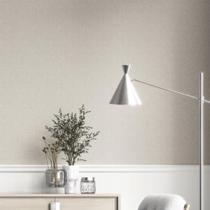May include: A room with a textured, neutral-toned wallpaper. A silver floor lamp with a conical shade stands to the right. A wooden cabinet displays vases and a glass jar. The room has a minimalist, modern design, with a light and airy feel.