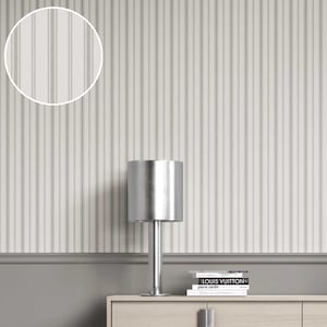 May include: A silver table lamp with a cylindrical shade sits on a light wood cabinet. The background features a white and gray striped wallpaper. Books are stacked on the cabinet. The wall has a gray trim.