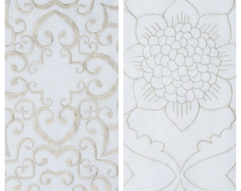 May include: Two white fabric panels with embroidered designs. The panel on the left has a repeating pattern of swirls and loops. The panel on the right has a large embroidered flower in the centre.
