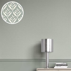 Könnte beinhalten: Eine Wand mit einem sich wiederholenden Muster aus kleinen, hellgrünen Rauten. Ein kreisförmiger Einsatz zeigt ein weißes und hellgrünes Blattdesign. Eine silberne Lampe steht auf einer hellen Holzoberfläche.