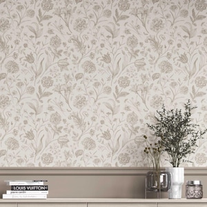 Może przedstawiać: Tapeta w kwiaty z powtarzającym się wzorem beżowych i szarobrązowych kwiatów i liści. Projekt zawiera różne rodzaje kwiatów i kształty liści, tworząc klasyczny, elegancki wygląd. Tapeta jest prezentowana na ścianie z ozdobną listwą i półką z książkami i wazonami.