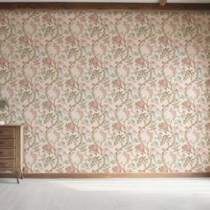 May include: A room with floral wallpaper in shades of pink, green, and beige. A wooden dresser with three drawers sits against the wall. A large window with a wooden frame is on the right side of the room. The floor is white.