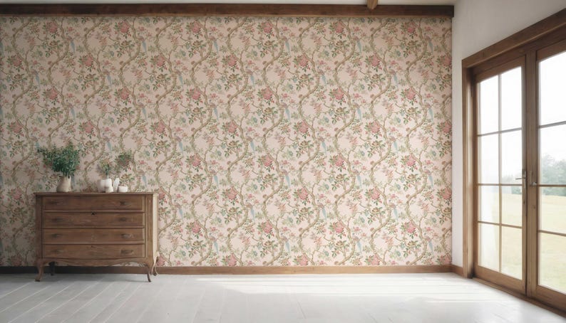 May include: A room with floral wallpaper in shades of pink, green, and beige. A wooden dresser with three drawers sits against the wall. A large window with a wooden frame is on the right side of the room. The floor is white.