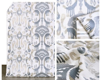 Può includere: Tessuto bianco con un motivo ikat ricamato grigio e beige. Il tessuto è mostrato in tre viste diverse, tra cui un primo piano della trama.