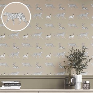 Pode incluir: Papel de parede com um padrão repetido de chitas e gazelas em preto e branco sobre um fundo bege. O design inclui um close-up de uma chita em uma moldura circular. Um elemento decorativo para design de interiores.