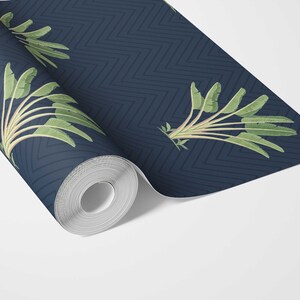 May include: A roll of navy blue wallpaper with a repeating chevron pattern. The wallpaper features a botanical design of green banana leaves and stems. The roll is partially unrolled, revealing the pattern and design.