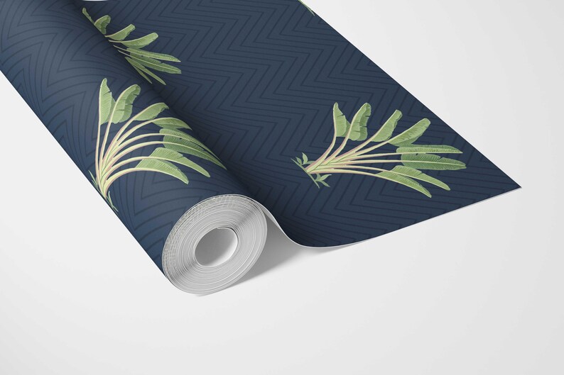 May include: A roll of navy blue wallpaper with a repeating chevron pattern. The wallpaper features a botanical design of green banana leaves and stems. The roll is partially unrolled, revealing the pattern and design.