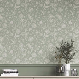 Op de afbeelding: Saliegroen behang met een wit bloemenpatroon. Het ontwerp toont verschillende bloemen en bladeren, waardoor een botanisch thema ontstaat. Het behang wordt getoond met decoratieve items, waaronder boeken en vazen.