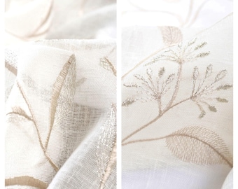 May include: Close-up of sheer white fabric with delicate embroidered floral designs in a light beige color.
