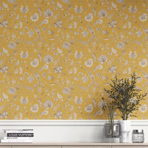 May include: Mustard yellow floral wallpaper with a repeating pattern of stylized flowers and leaves in shades of gray and white. The wallpaper is displayed on a wall with a white baseboard and a wooden shelf with decorative items.
