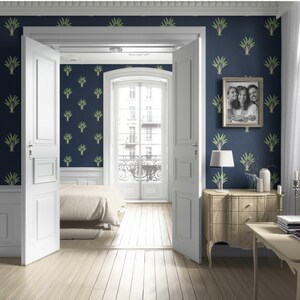 May include: A bedroom interior with navy blue walls adorned with a green leaf pattern. White doors open to a light-filled balcony. A framed family photo hangs above a wooden dresser with a lamp. The room features light wood flooring and a bed.