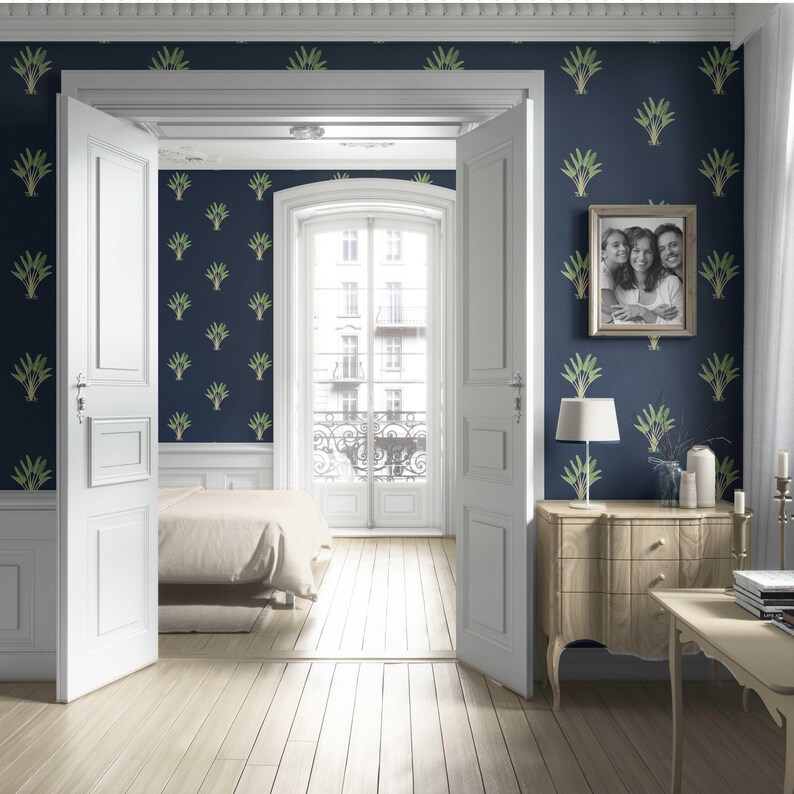 May include: A bedroom interior with navy blue walls adorned with a green leaf pattern. White doors open to a light-filled balcony. A framed family photo hangs above a wooden dresser with a lamp. The room features light wood flooring and a bed.