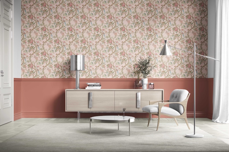 May include: A modern living room with floral wallpaper, a light wood cabinet, and a gray chair. A silver lamp and a floor lamp provide lighting. The room has a neutral color palette with accents of coral.