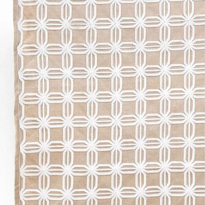 May include: A beige throw blanket with a white embroidered geometric pattern. The pattern is a repeating design of interlocking circles and squares.