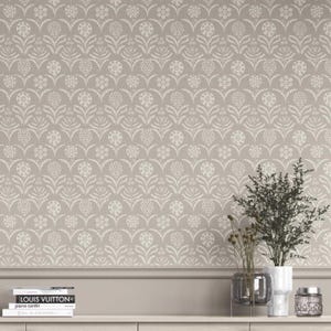 May include: A taupe wallpaper featuring a repeating white floral pattern with arched lines. Below the wallpaper is a taupe wainscoting ledge holding a stack of books labeled Pierre Cardin, a glass vase with green foliage, and a small glass jar.