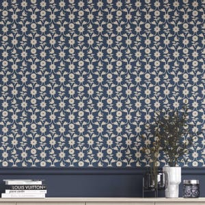May include: Navy blue wallpaper with a cream floral pattern. The design features stylized flowers and leaves. The wallpaper is installed on a wall above a dark blue baseboard. Decorative items are on a white shelf.