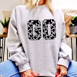 May include: A gray sweatshirt with a black and white cow print "GO" graphic.