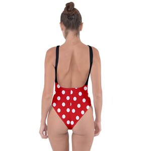 May include: Red swimsuit with white polka dots and black straps. The one-piece has a scoop back and is made of a stretchy material. The swimwear is designed for swimming and sunbathing.