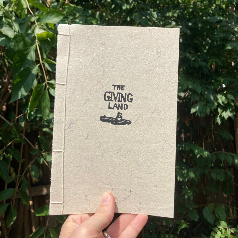 May include: A book with a white cover and the title "The Giving Land" printed in black.