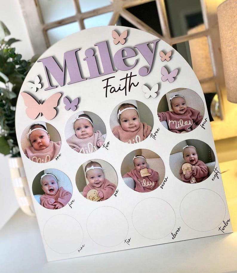 May include: A white wooden arch with the names "Miley Faith" in purple lettering. The arch has 12 circles with photos of a baby girl at different ages. Each circle has a number from one to twelve written below it.