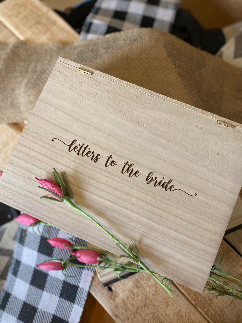 Puede incluir: Una caja de madera con las palabras "cartas para la novia" grabadas en la tapa. La caja est&aacute; decorada con una rama de flores rosas.