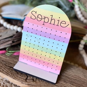 May include: A rainbow-colored wooden earring holder with a unicorn silhouette and the name "Sophie" printed on it.