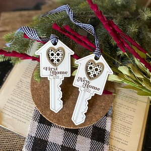 May include: Two wooden key-shaped ornaments with a house design and a heart cutout. The top ornament says "First Home 2022" and the bottom ornament says "New Home 2022".